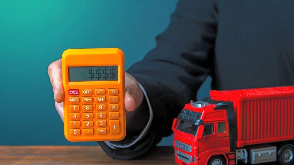 Simulação de preço de mudança: messoa seguirando uma calculadora laranja com uma miniatura de caminhão encima da mesa.