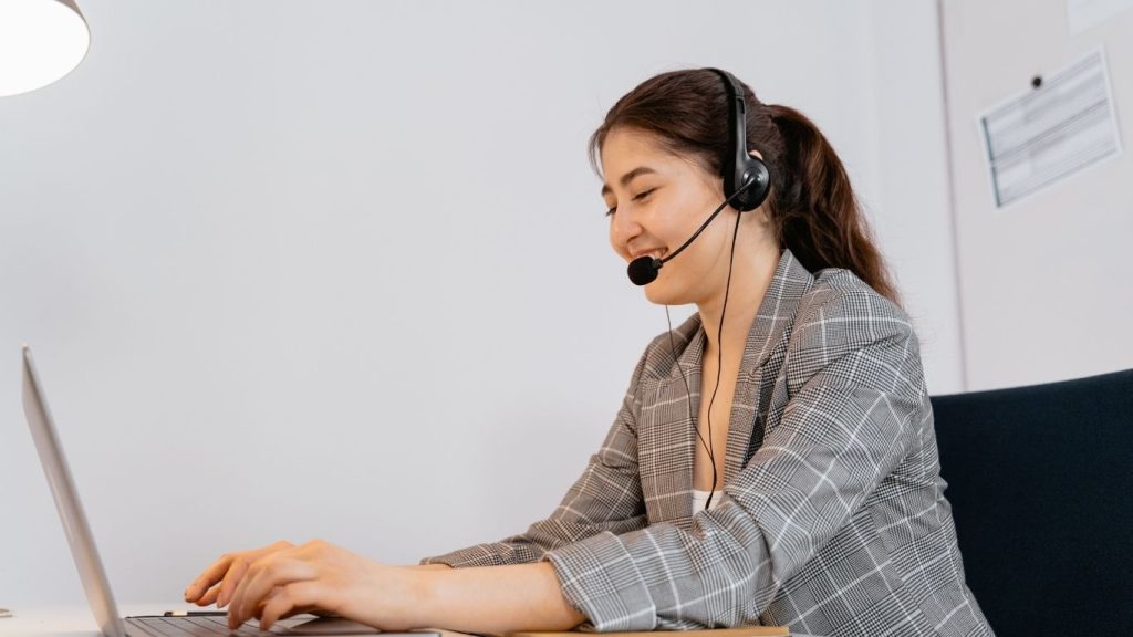 mulher com fone de ouvido que tem microfone mexendo eu seu notebook enquanto trabalha.