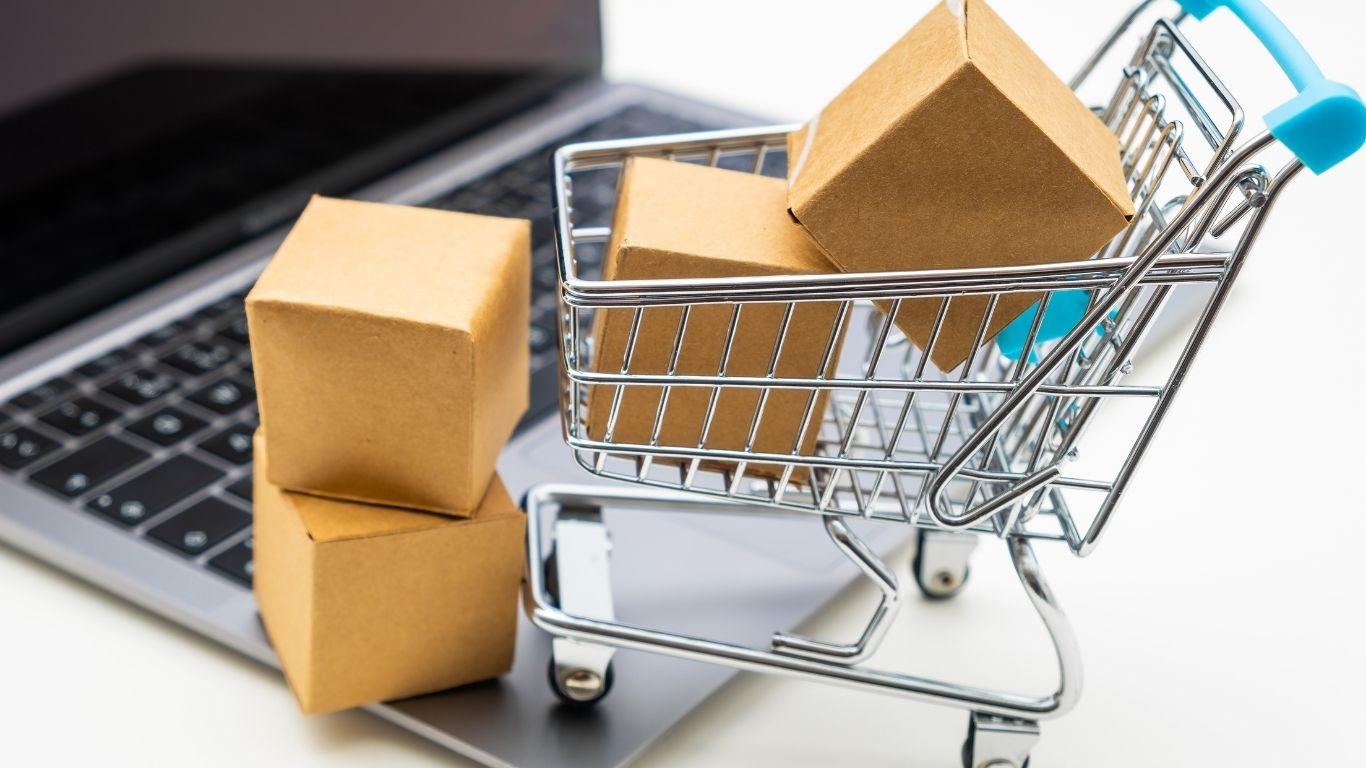 Onde comprar caixas de papelão para mudança: miniatura de carrinho com caixas dentro e na frente do lado de fora e ambos encima de um notebook.