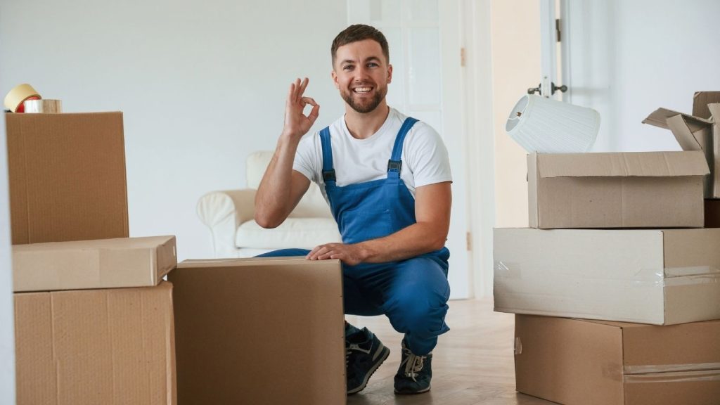 Empresa de mudanças em Santa Luzia: funcionário de empresa de mudança fazendo sinal de ok com as mãos em volta de caixas com mudança.
