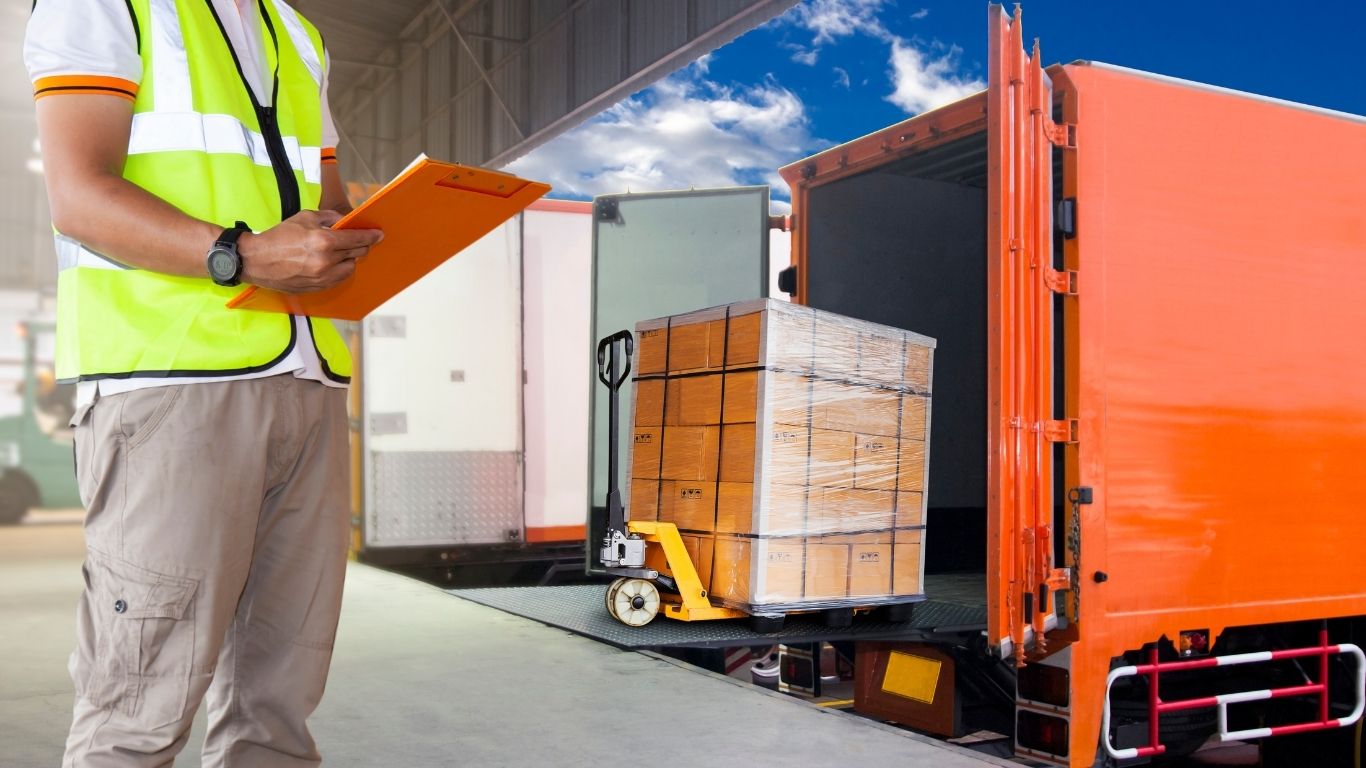 pessoa preenchendo documento e carga sendo colocada em caminhão.